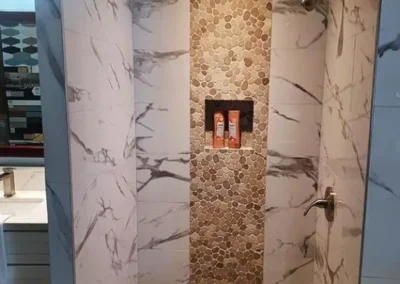Modern shower with marble tiles and a pebble-stone accent wall