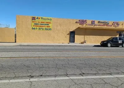 Street view of a one-story yellow commercial building with flooring business signs and parked cars